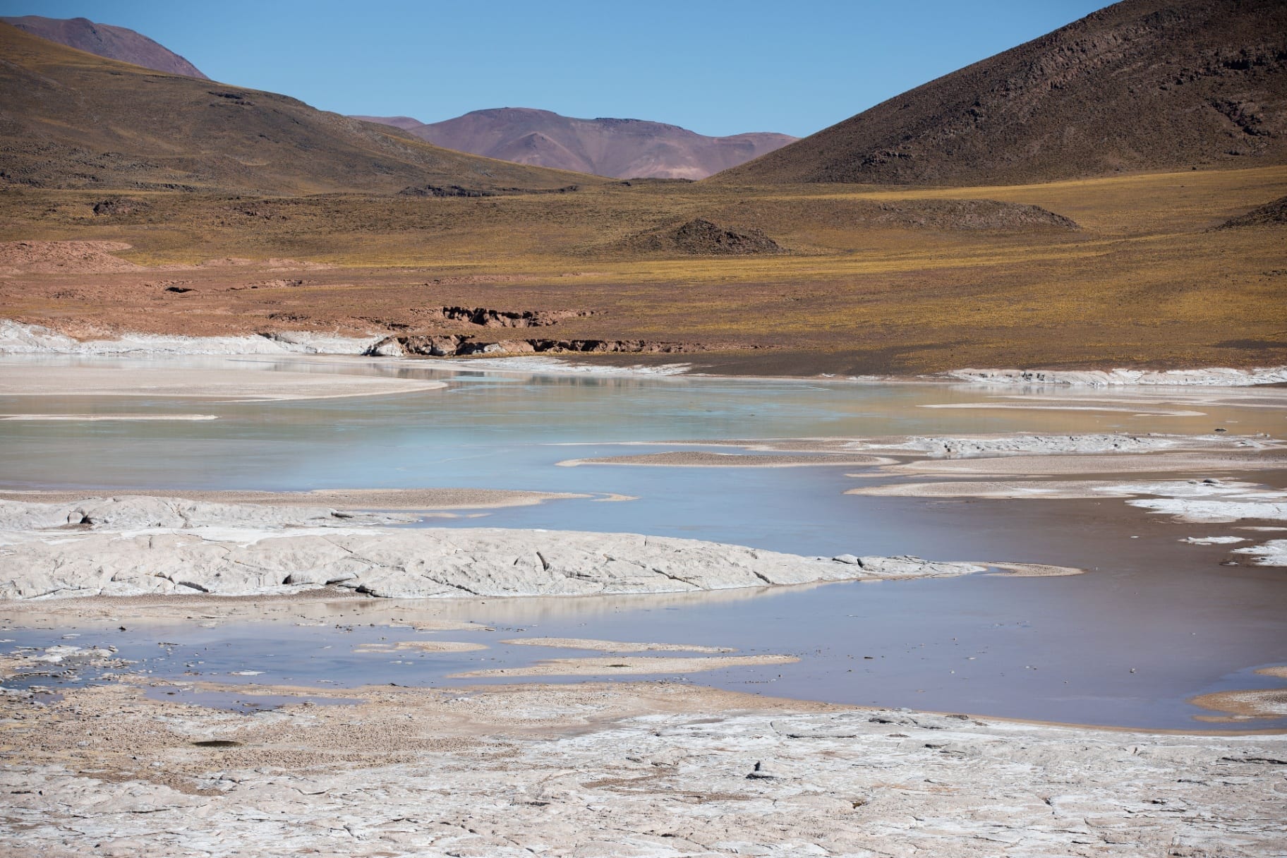 Laguna azul com crostas de sal e montanhas ao fundo