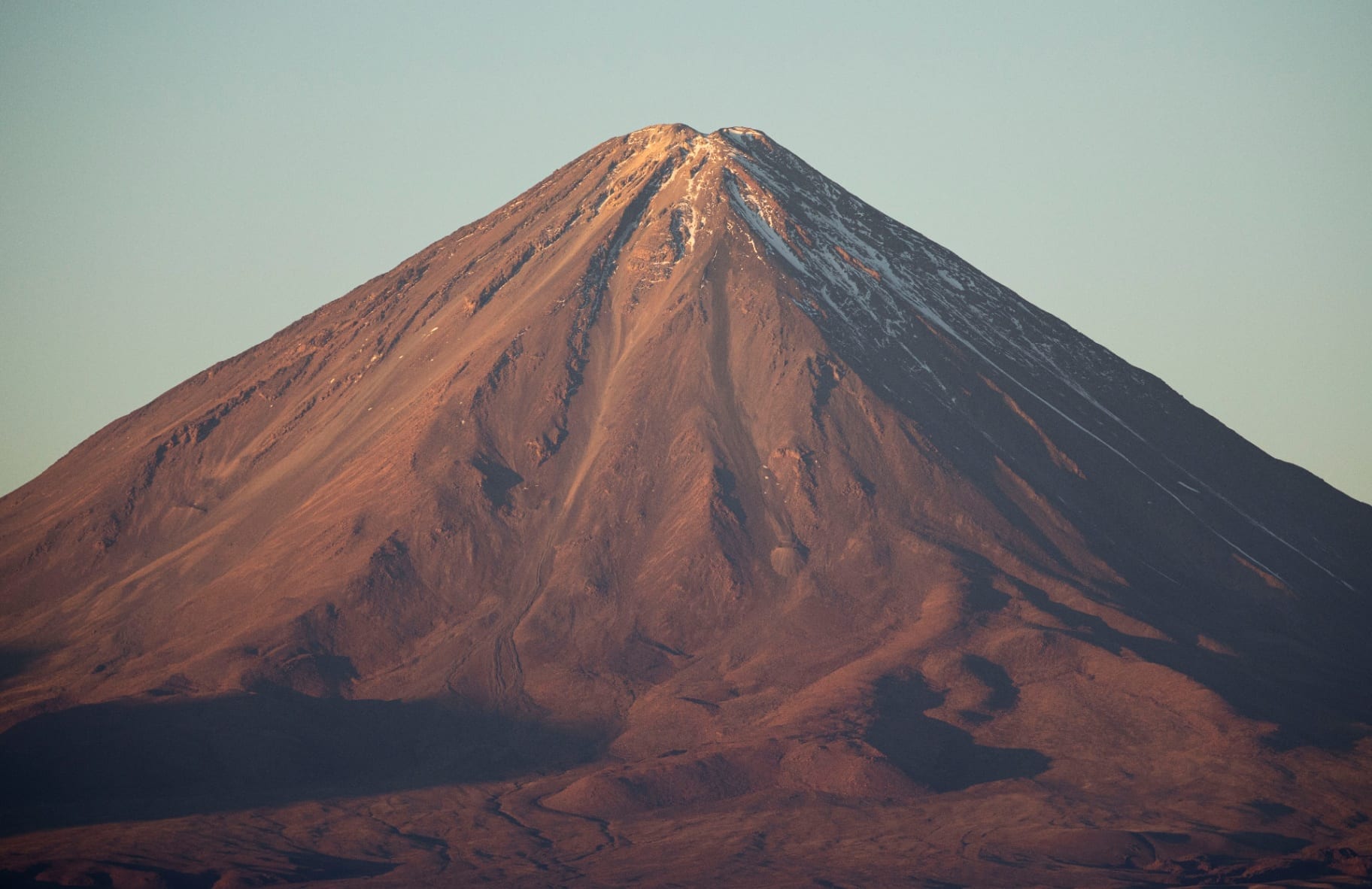 Vulcão Licancabur ao entardecer com tons cobre e neve