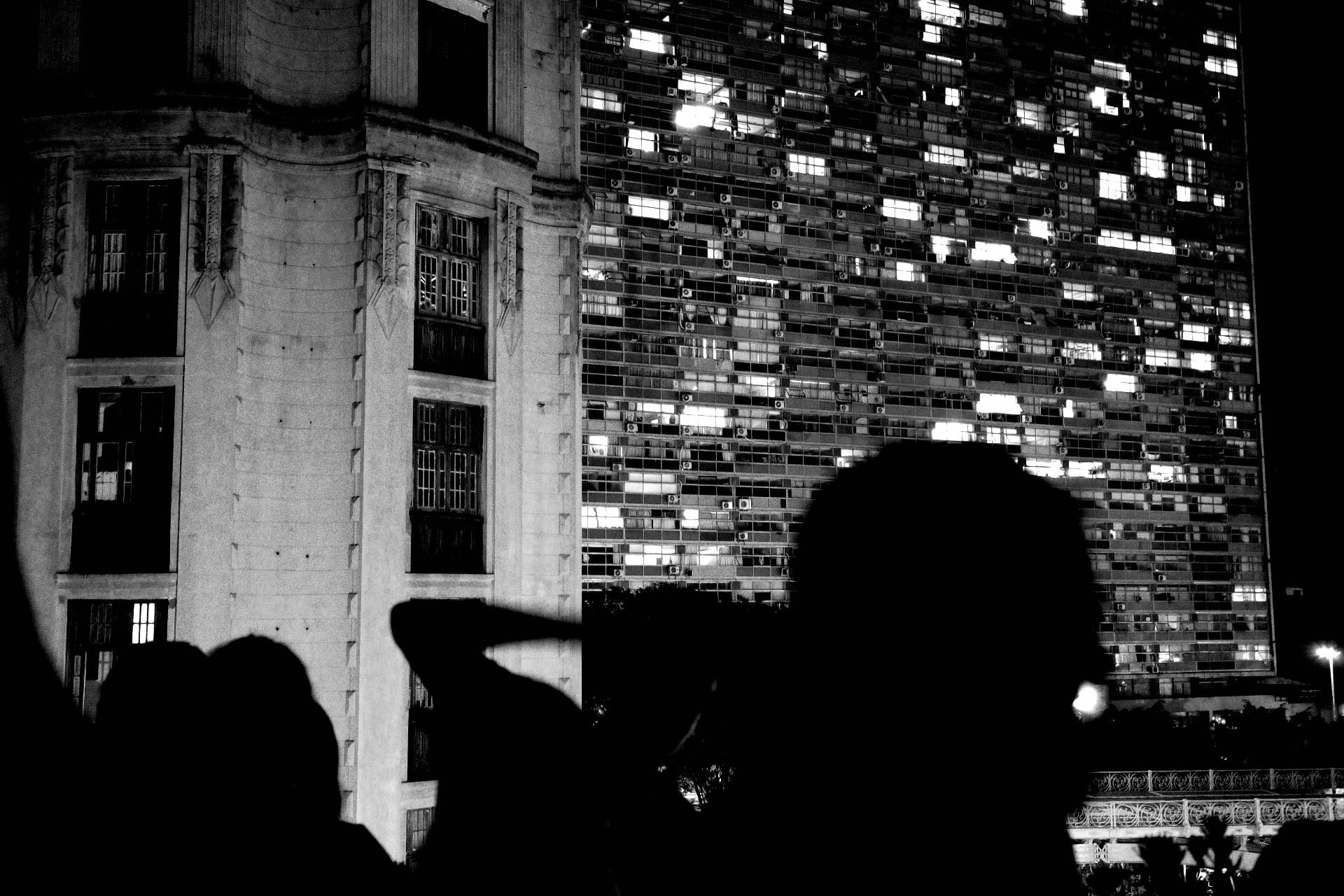 Silhuetas diante de edifício iluminado à noite