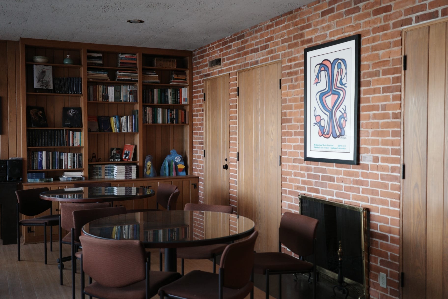 Mesas redondas, estante de livros e parede de tijolo junto à lareira