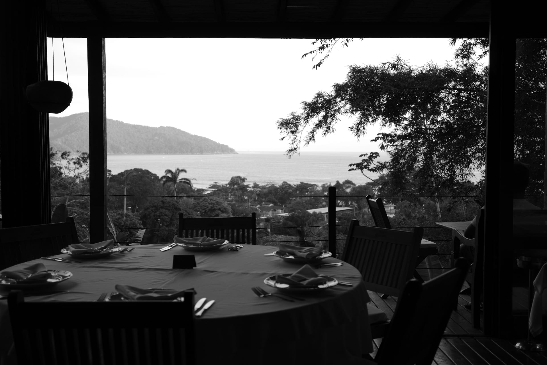 Mesa posta sob varanda aberta com vista para o mar e a mata